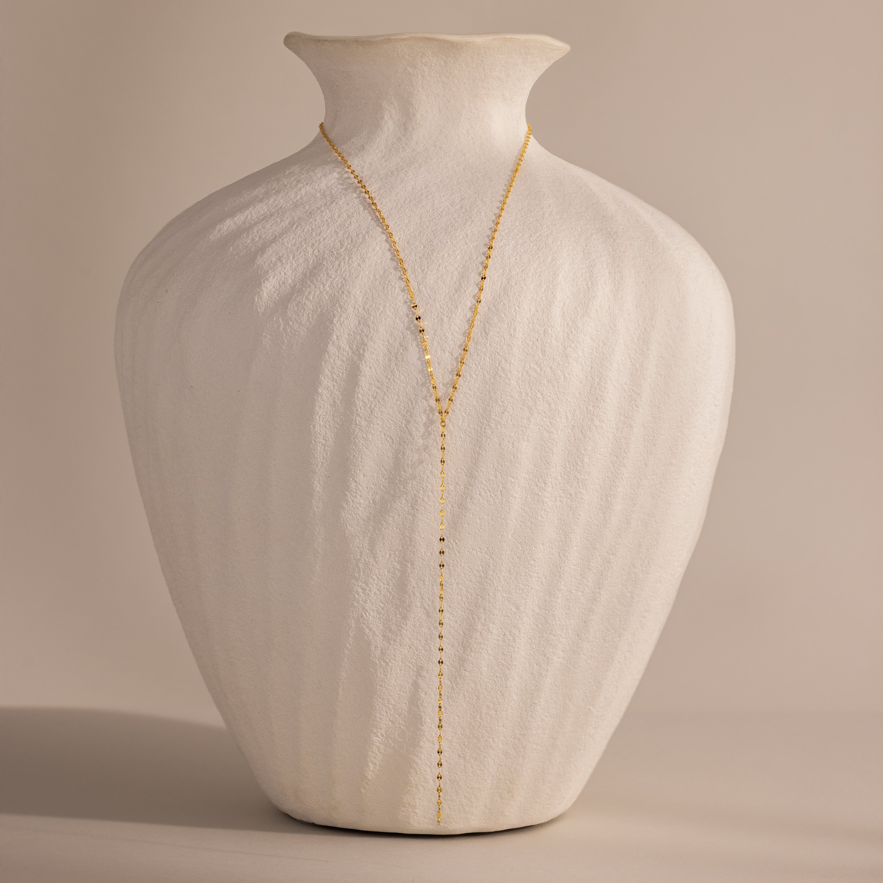 Gold dainty mirror chain lariat necklace displayed on a white ceramic vase.