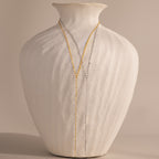 A white textured vase displays two delicate necklaces, including the Mirror Chain Lariat Necklace with a reflective finish, elegantly draped over the front.