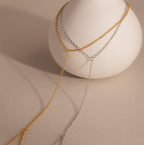 The Dainty Hand Chain Bracelet in 18K Gold is elegantly displayed over a smooth white vase on a beige background, perfect for anyone who loves delicate, minimalist jewelry.
