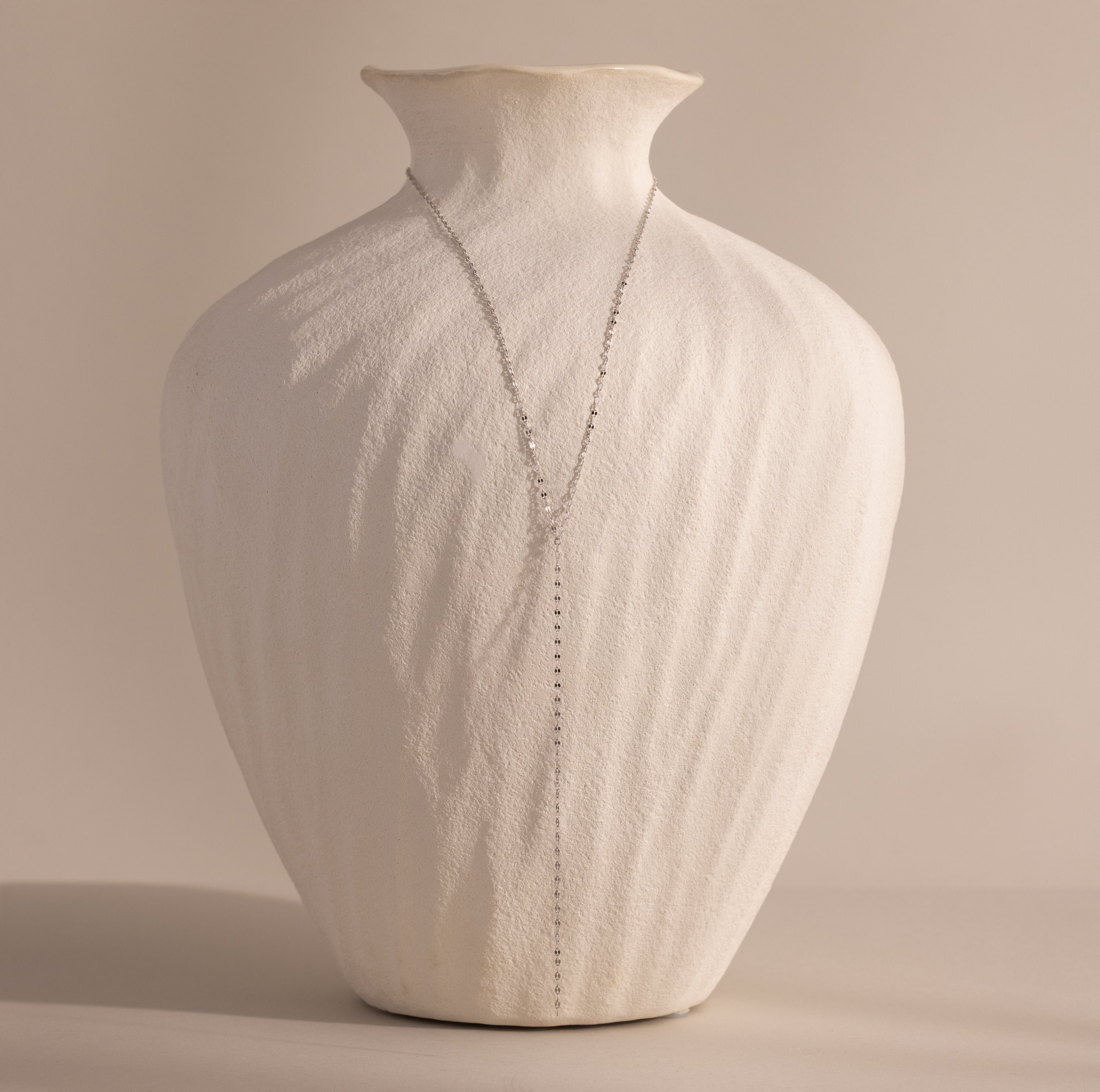 Silver mirror chain lariat necklace displayed against a white vase.
