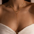 Model wearing a gold dainty mirror chain lariat necklace, layered with a gold necklace with an arc-shaped charm featuring an emerald birthstone.