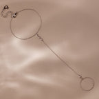 A silver hand chain bracelet with delicate diamonds laid flat on a beige surface with soft shadows.