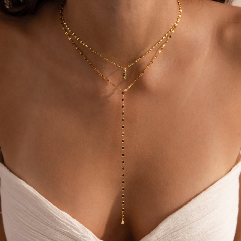 Model wearing a gold dainty Sparkling Diamond Lariat Necklace, layered with a marquise peridot birthstone necklace.