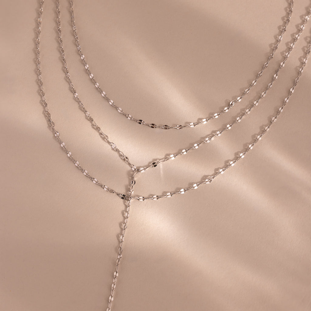 Close-up of a silver dainty Sparkling Layered Lariat Necklace, featuring 3 layers of mirror chain necklaces in varying lengths.