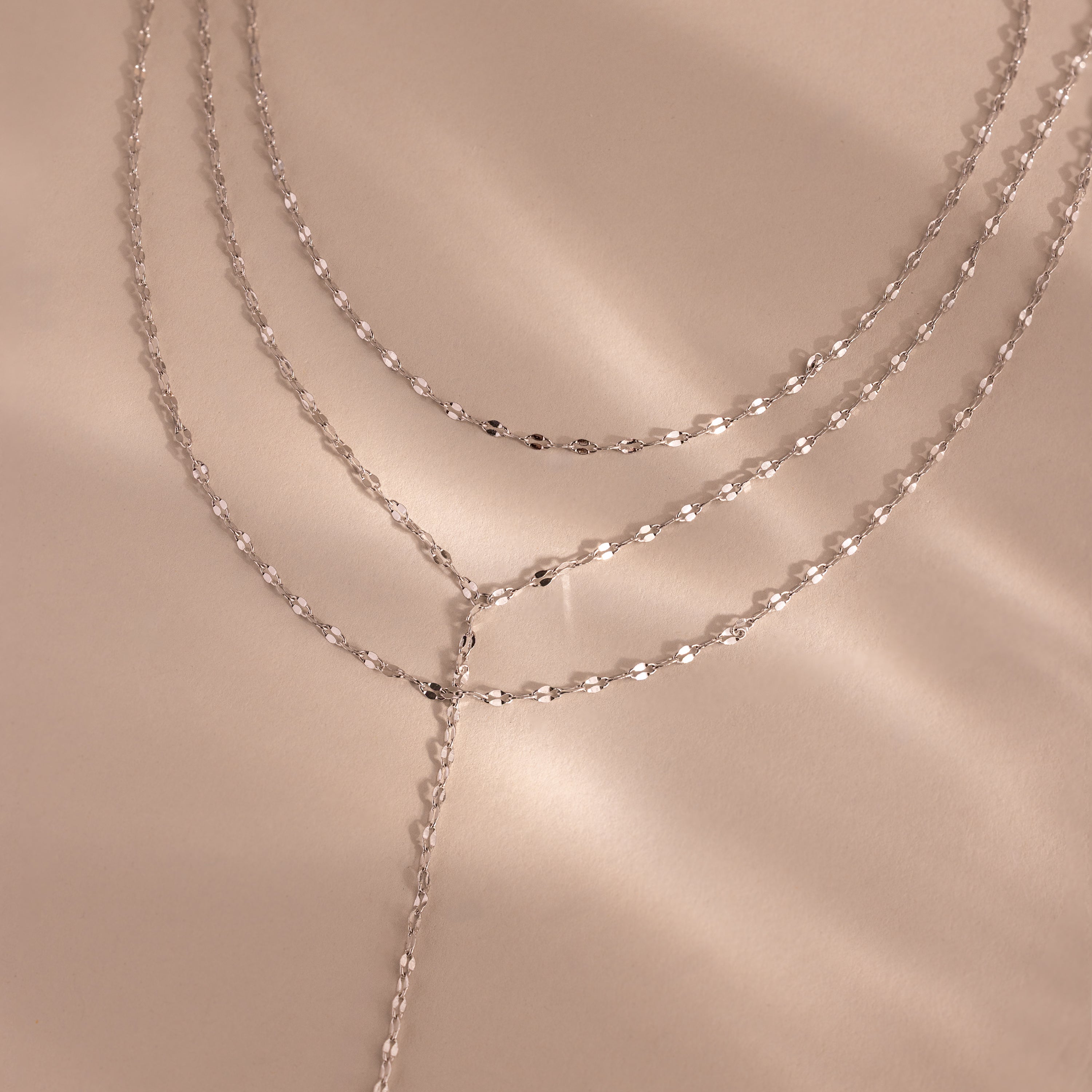 Close-up of a silver dainty Sparkling Layered Lariat Necklace, featuring 3 layers of mirror chain necklaces in varying lengths.