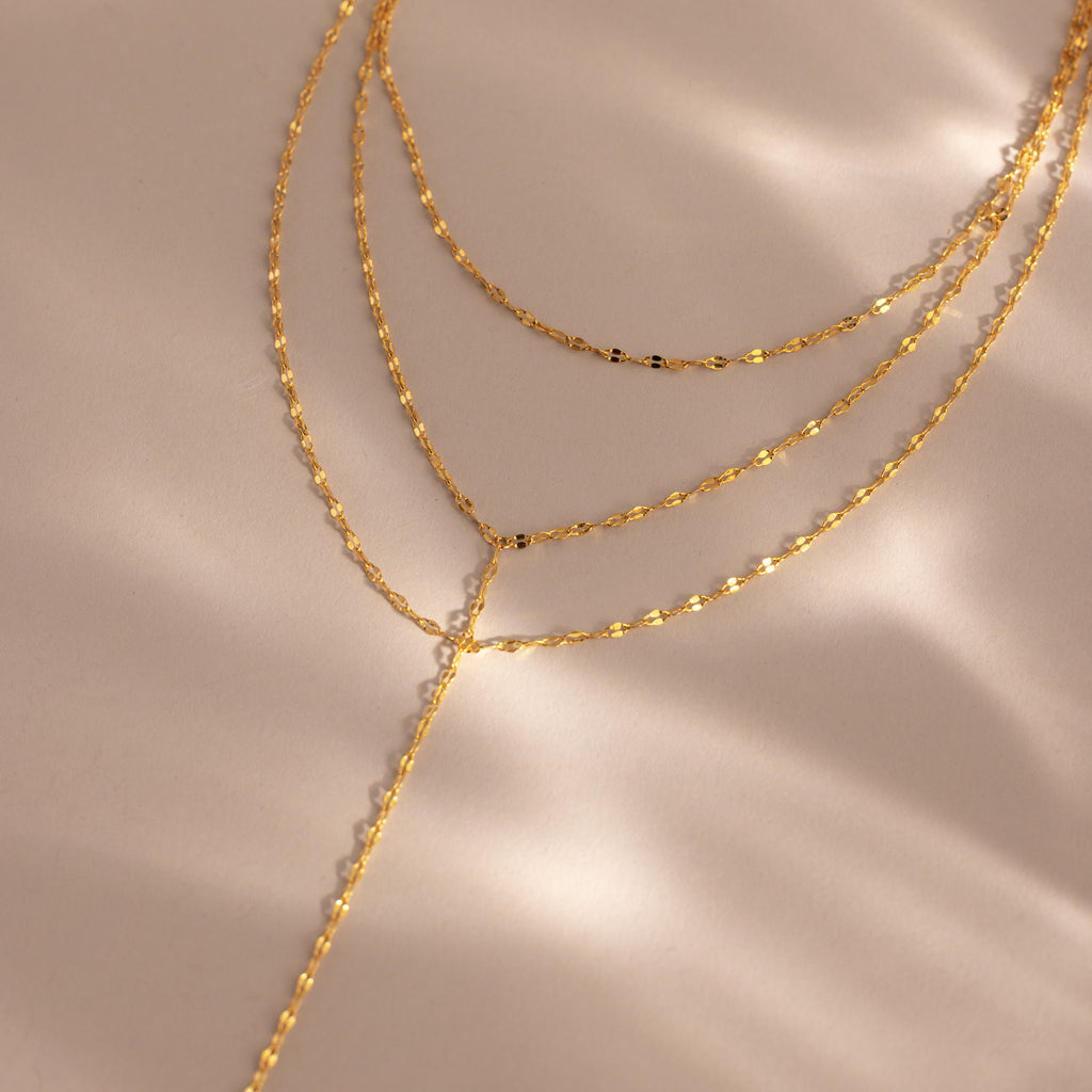 Close-up of a gold dainty Sparkling Layered Lariat Necklace, featuring 3 layers of mirror chain necklaces in varying lengths.