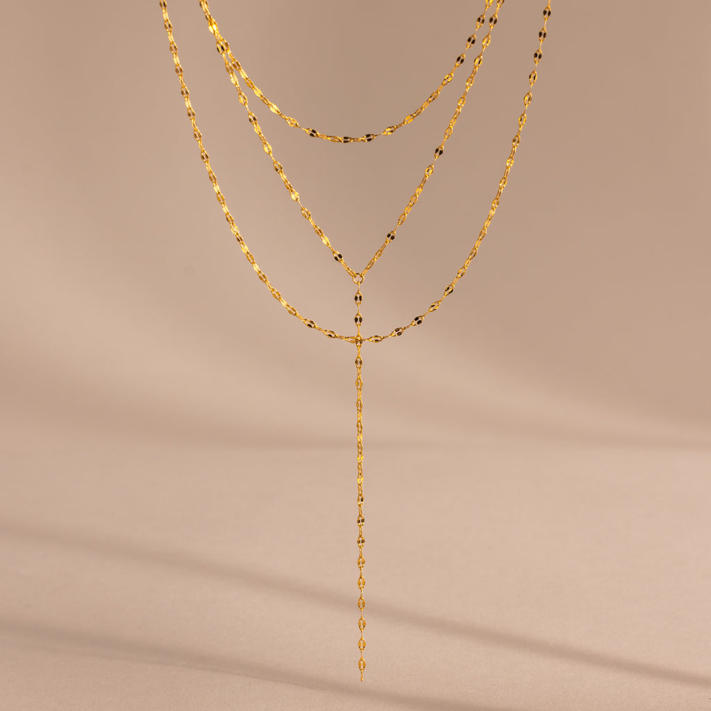 Close-up of a gold dainty Sparkling Layered Lariat Necklace, featuring 3 layers of mirror chain necklaces in varying lengths.