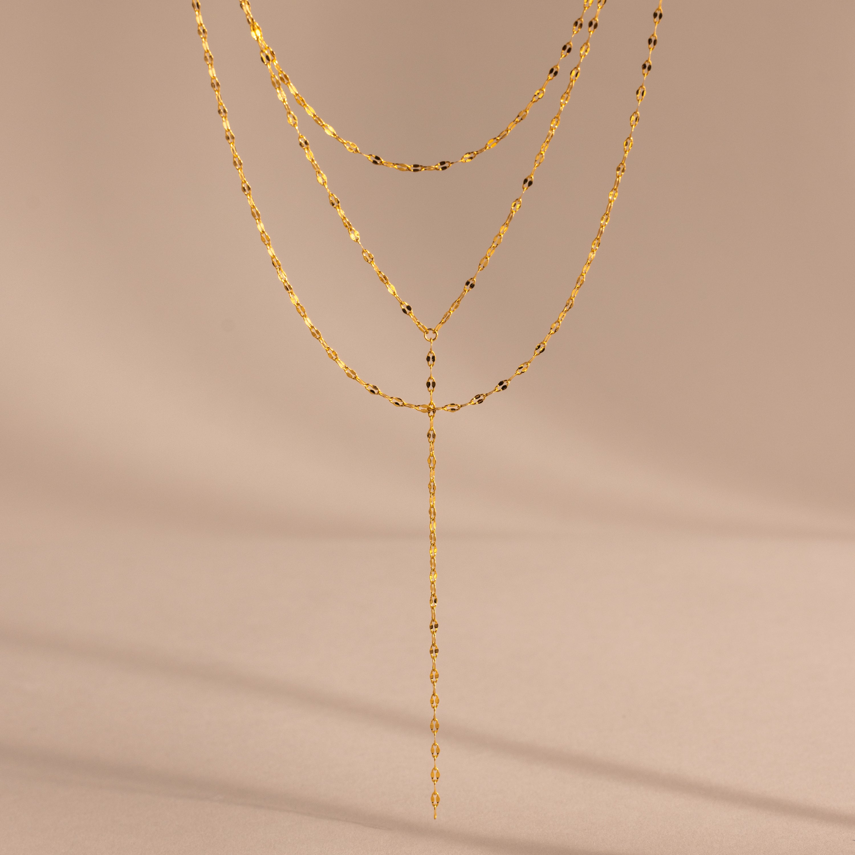 Close-up of a gold dainty Sparkling Layered Lariat Necklace, featuring 3 layers of mirror chain necklaces in varying lengths.