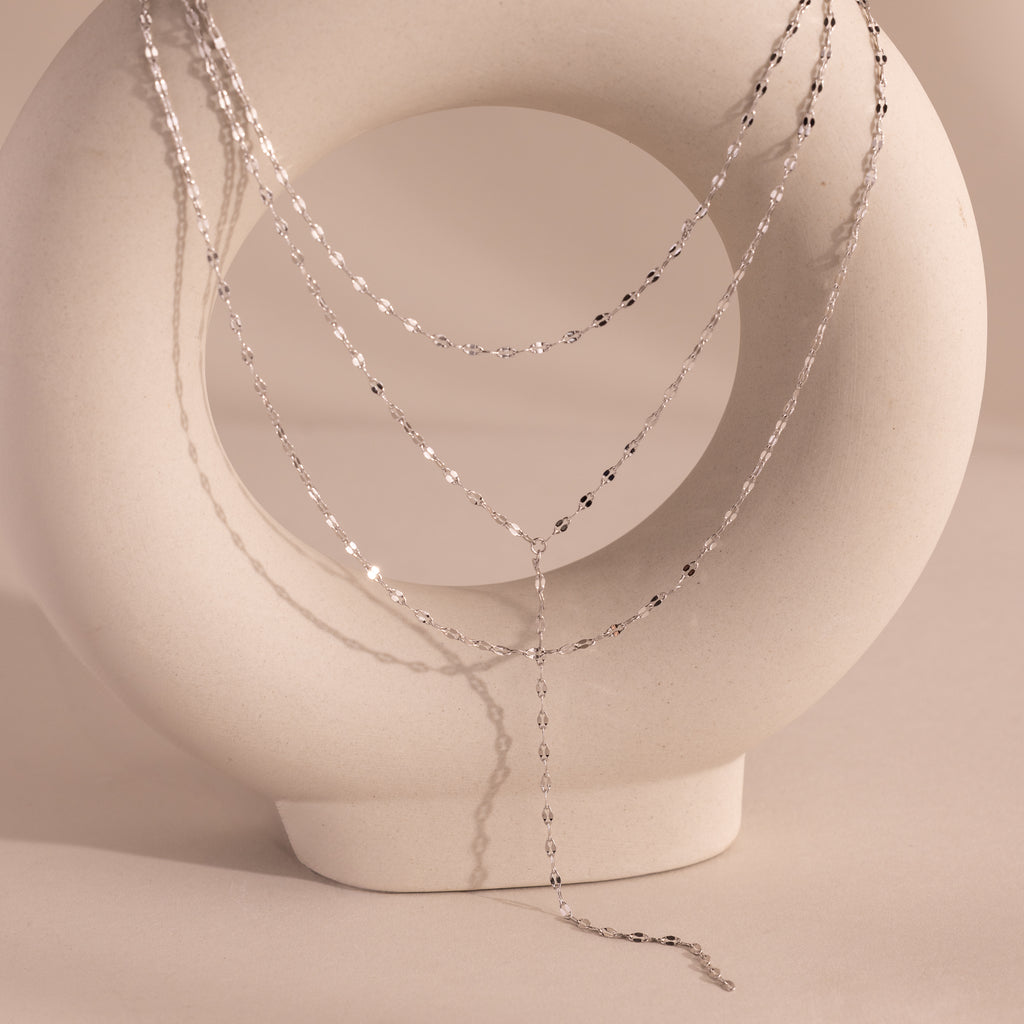 Silver dainty Sparkling Layered Lariat Necklace, featuring 3 layers of mirror chain necklaces in varying lengths, displayed on a ceramic prop.