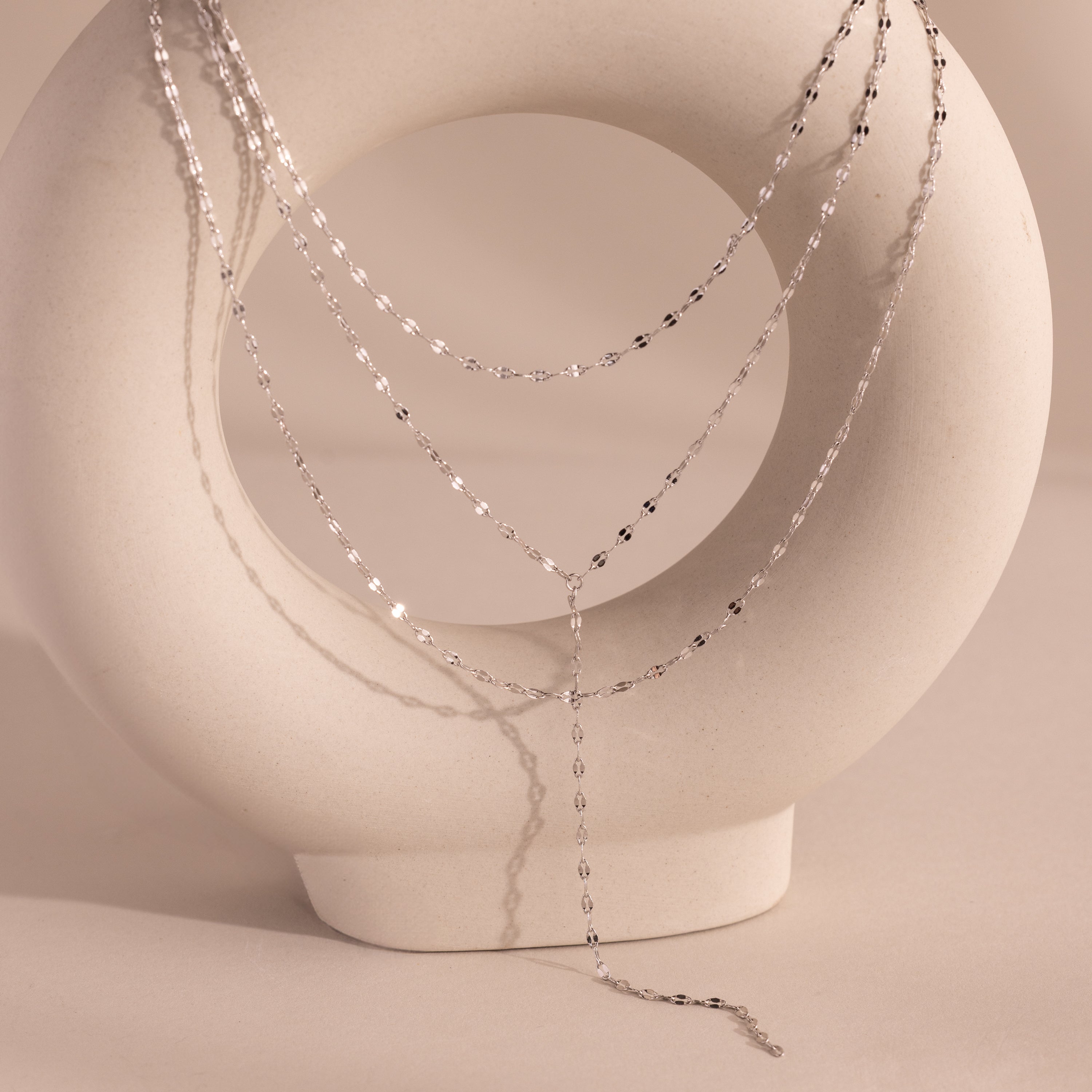 Silver dainty Sparkling Layered Lariat Necklace, featuring 3 layers of mirror chain necklaces in varying lengths, displayed on a ceramic prop.