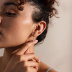 A woman touches her Diamond Drop Huggies in Sterling Silver, her face partially visible in gentle, natural light.