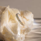 The White Opal Inlay Band in Sterling Silver rests on a rough, pale crystal surface, its iridescent sheen capturing the ethereal beauty of gemstone jewelry.