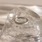 The White Opal Inlay Band in Sterling Silver shines on a clear, textured glass surface, with gentle light reflections enhancing the elegance of this gemstone jewelry.