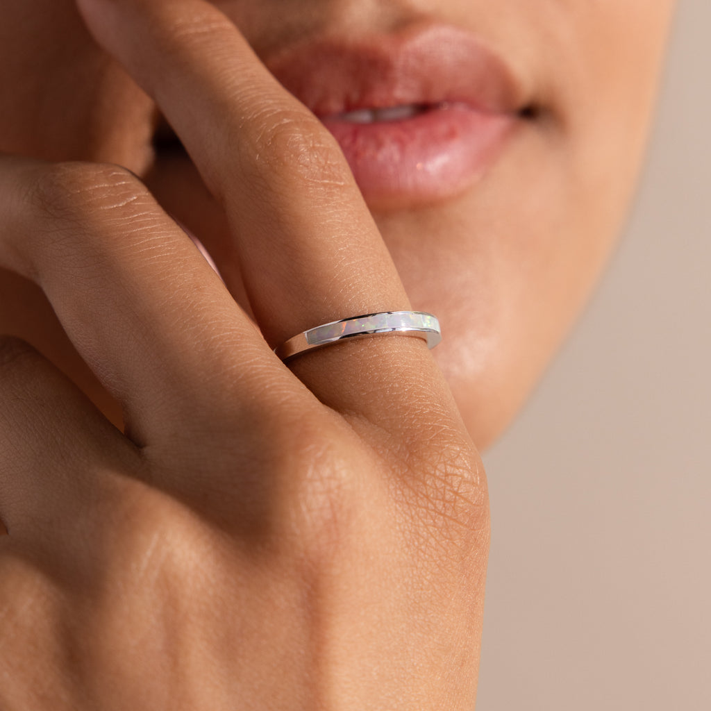 A close-up of a hand wearing the White Opal Inlay Band in Sterling Silver, fingers softly touching the lips to highlight the ring’s subtle iridescence.