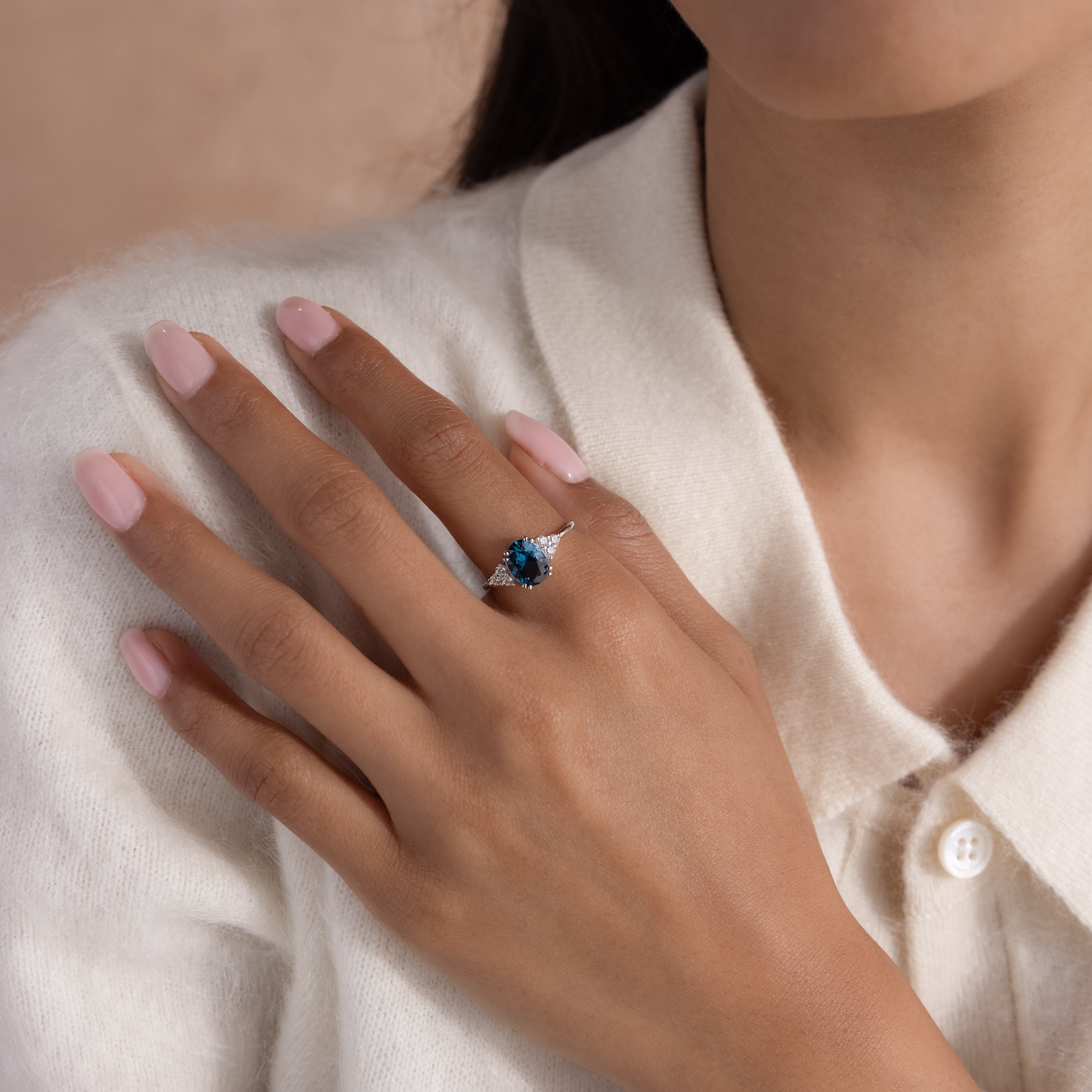 A woman in a cream sweater displays the Elizabeth Blue Topaz Ring in Sterling Silver—a vintage boho piece with a striking blue gemstone—on her finger.
