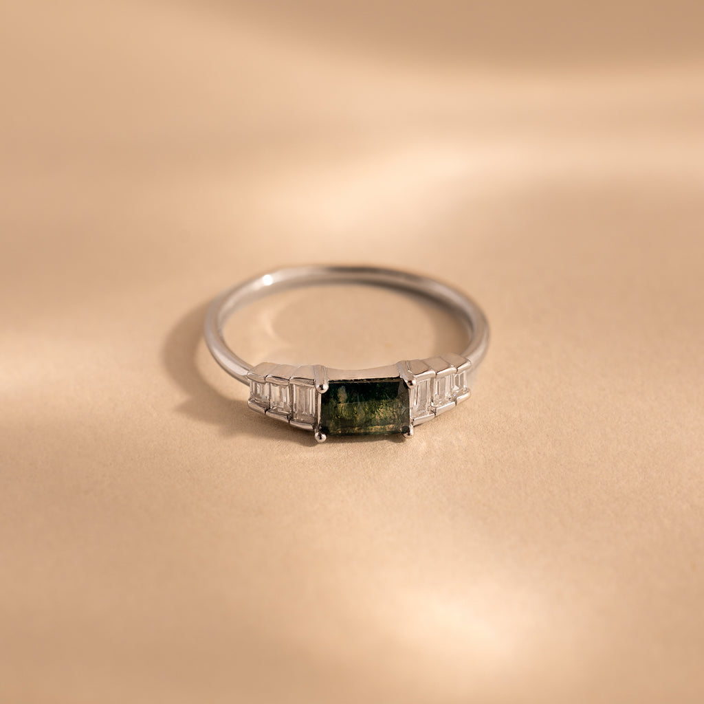 The ring lies flat on a neutral beige surface, emphasizing the clean, minimalist profile of the sterling silver band and the layered structure of the rectangular stones.