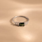 The ring lies flat on a neutral beige surface, emphasizing the clean, minimalist profile of the sterling silver band and the layered structure of the rectangular stones.
