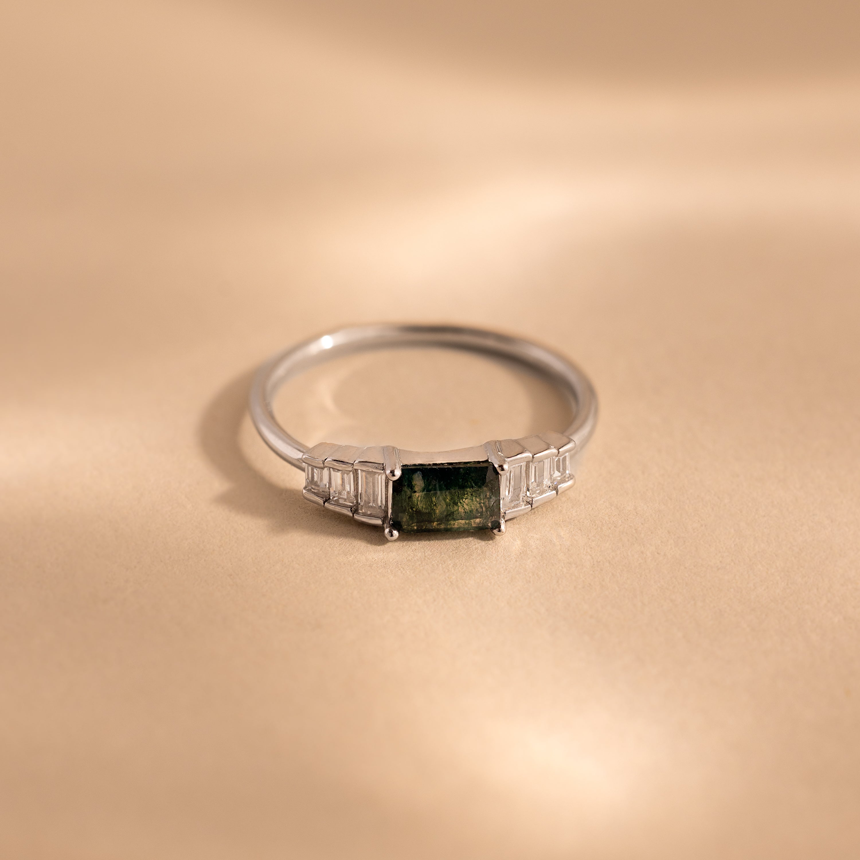 The ring lies flat on a neutral beige surface, emphasizing the clean, minimalist profile of the sterling silver band and the layered structure of the rectangular stones.