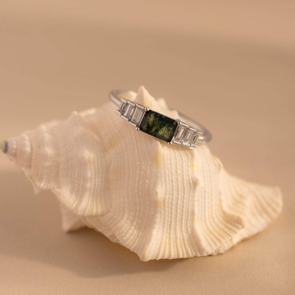 The silver agate ring is perched on a textured white seashell