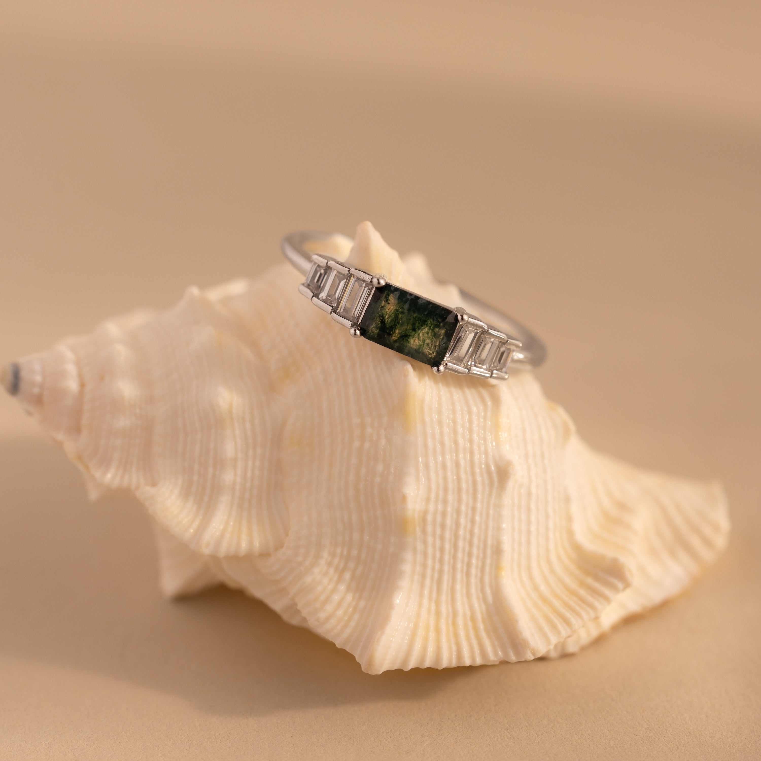 The silver agate ring is perched on a textured white seashell