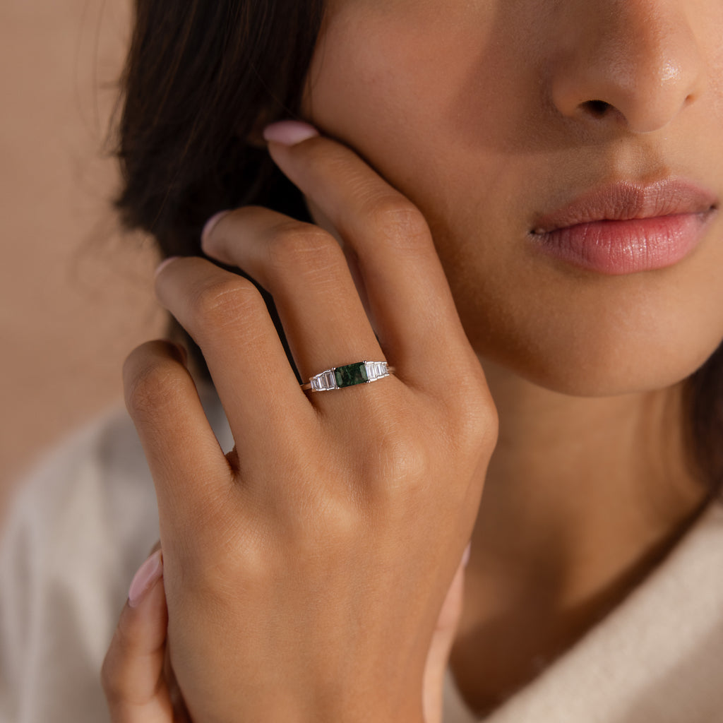 A woman gently touching her face while wearing the ring, showing how the piece sits elegantly on the hand. The deep green agate and clear baguettes catch soft light, offering a refined and natural look.