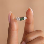 The ring is held delicately between two fingers against a soft peach-toned background. The elevated view showcases the symmetrical stone setting and the glossy finish of the sterling silver.