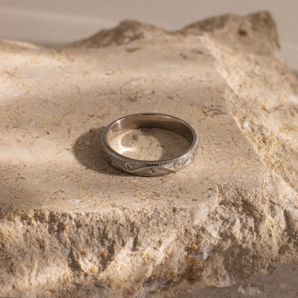 The Filigree Ring in Sterling Silver, featuring vintage-inspired intricate detailing, is displayed on a rough beige stone surface under soft lighting.