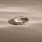 The Filigree Ring in Sterling Silver, featuring vintage-inspired engraved patterns, rests on a smooth, light surface under soft lighting.