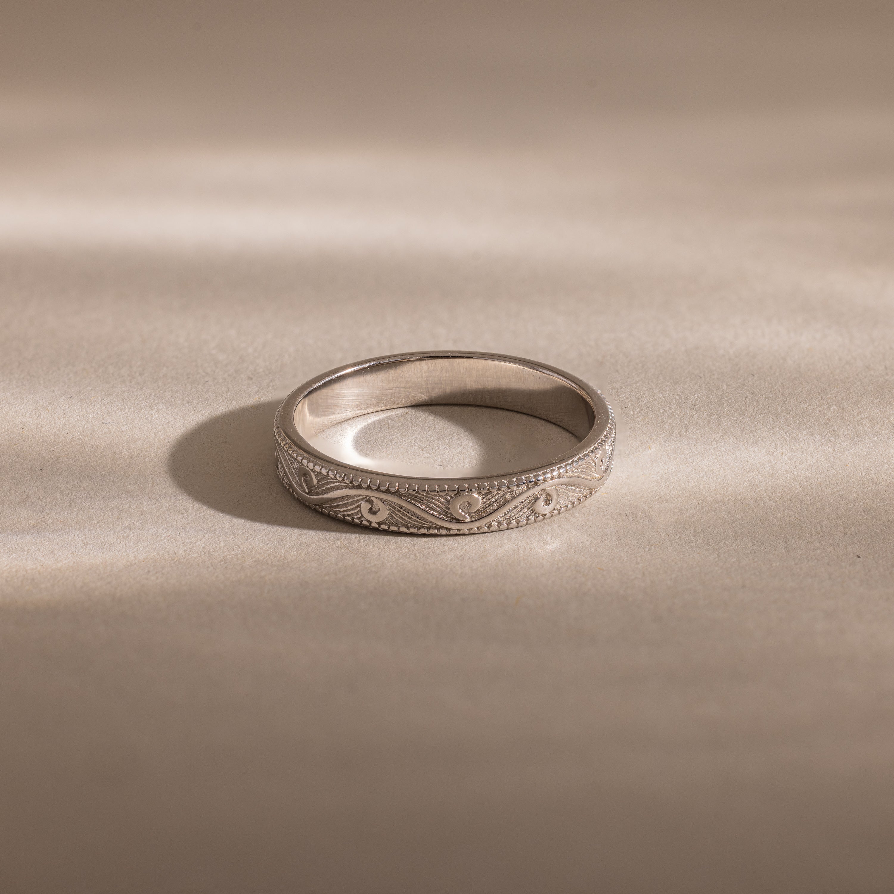 The Filigree Ring in Sterling Silver, featuring vintage-inspired engraved patterns, rests on a smooth, light surface under soft lighting.