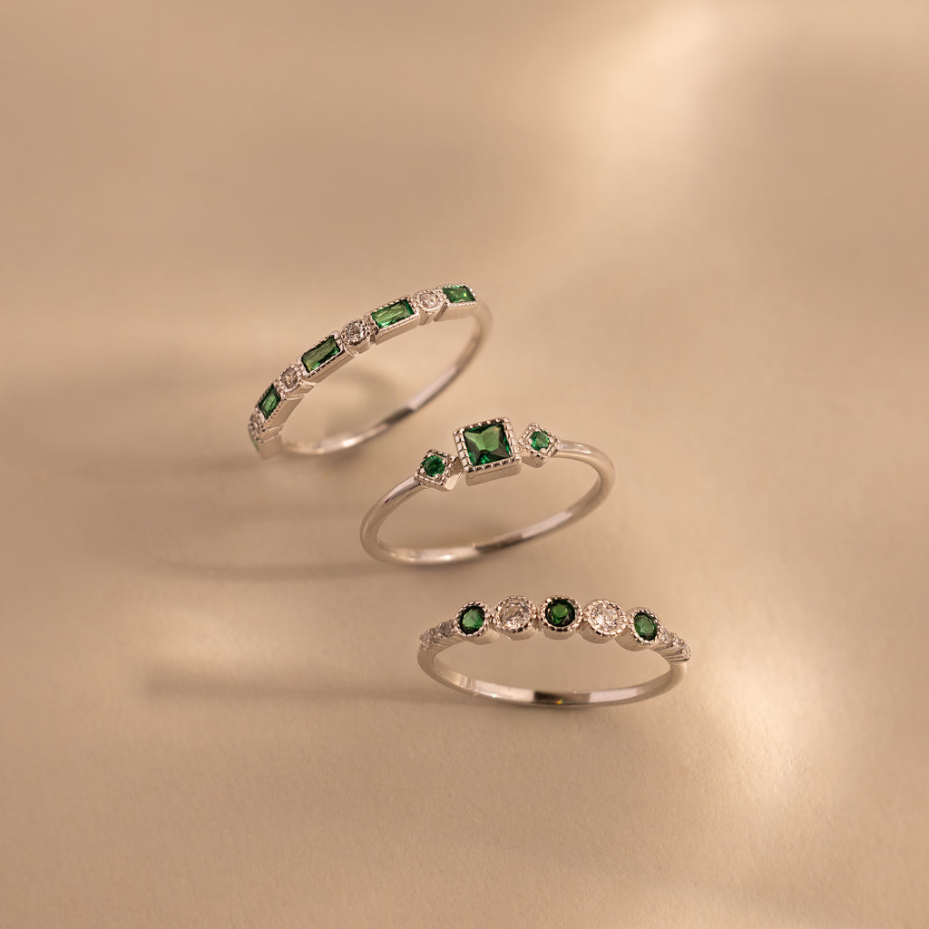 Three sterling silver rings from the Emerald Stacking Ring Set are displayed on a beige surface, showcasing green and white gemstones and offering a vintage-inspired art deco jewelry look.