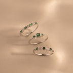 Three sterling silver rings from the Emerald Stacking Ring Set are displayed on a beige surface, showcasing green and white gemstones and offering a vintage-inspired art deco jewelry look.