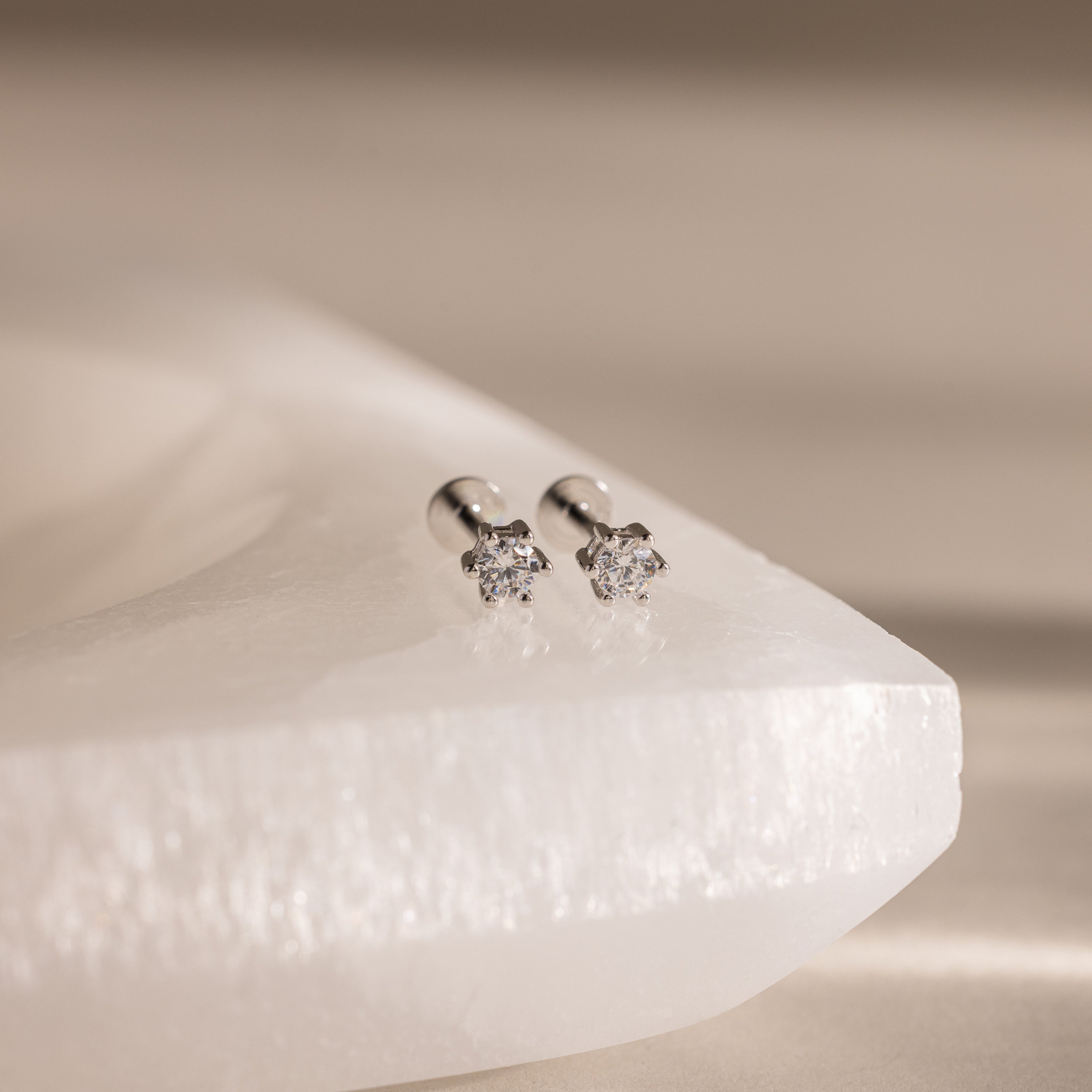 Diamond Flatback Studs shown with silver settings on a smooth white stone surface.