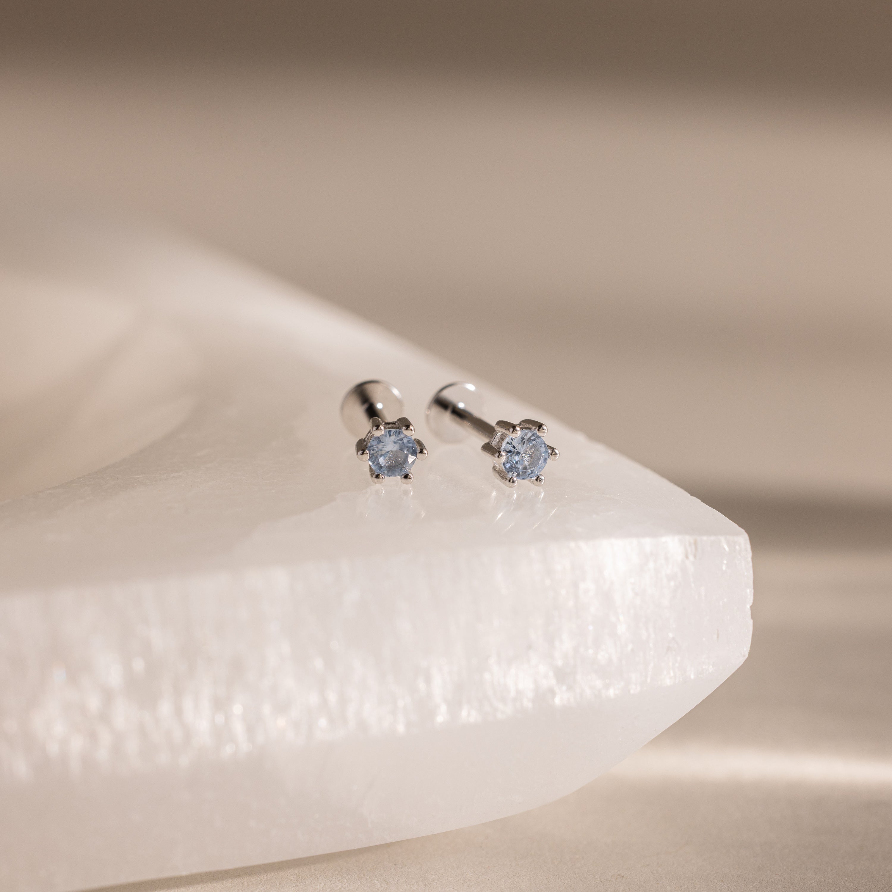 Aquamarine Flatback Studs: Silver stud earrings featuring small light blue aquamarines, perfect as birth month jewelry. Displayed on a white textured surface.
