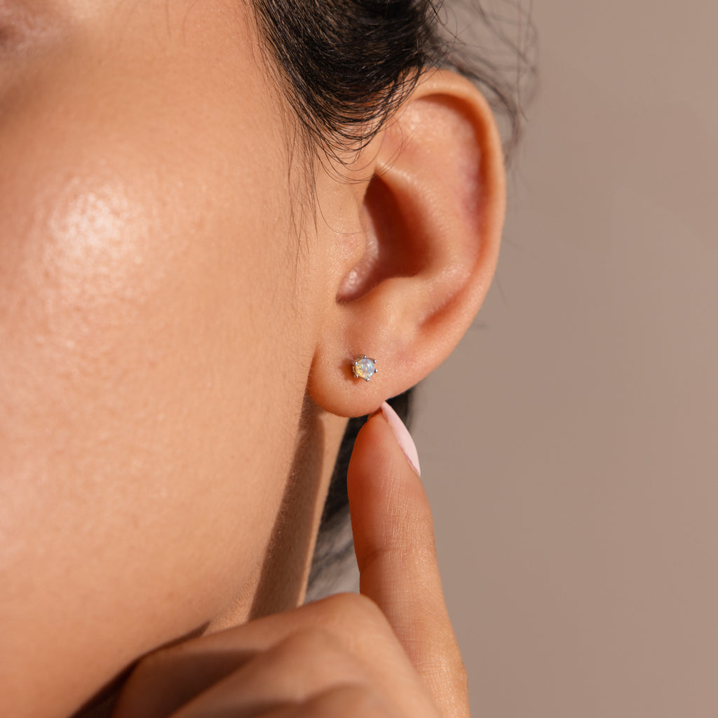 A close-up shows a person wearing Birthstone Flatback Studs, lightly touching their earlobe with a finger.