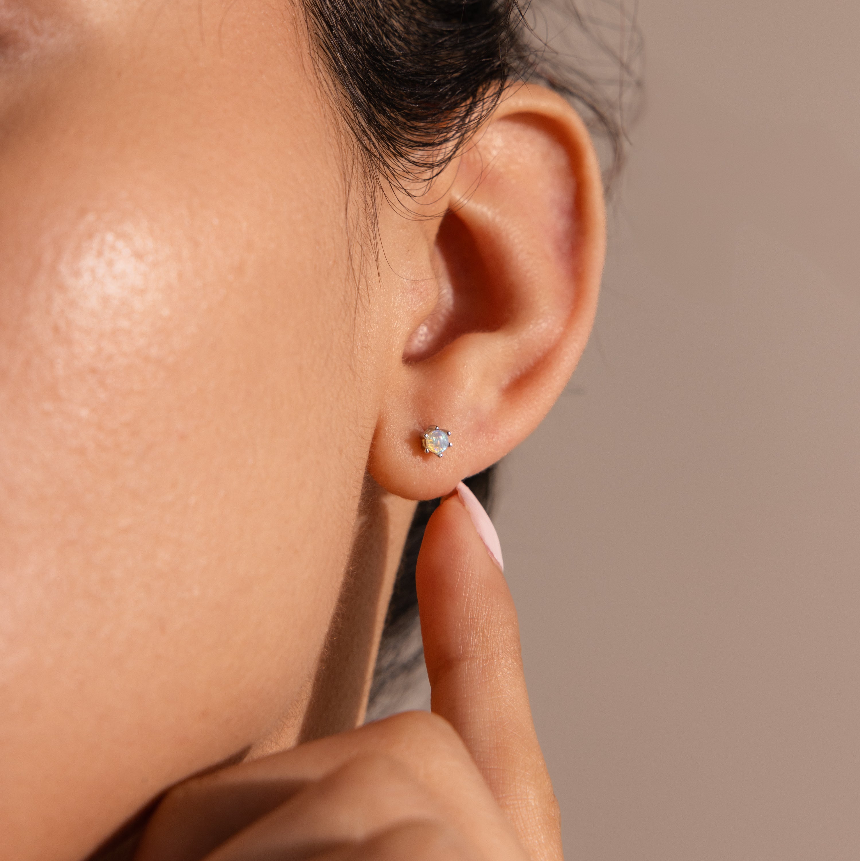 A close-up shows a person wearing Birthstone Flatback Studs, lightly touching their earlobe with a finger.