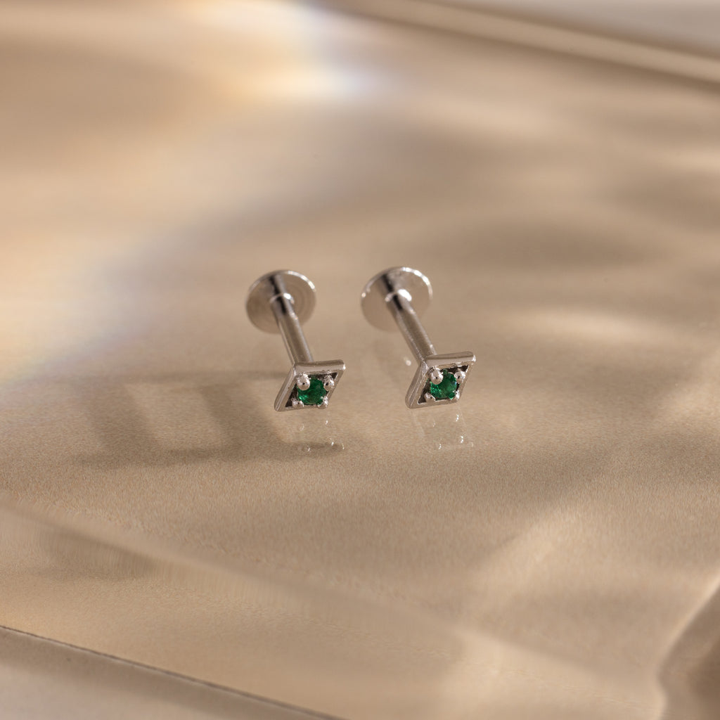 Pair of silver geometric flat back emerald stud earrings on a reflective surface