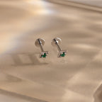 Pair of silver geometric flat back emerald stud earrings on a reflective surface