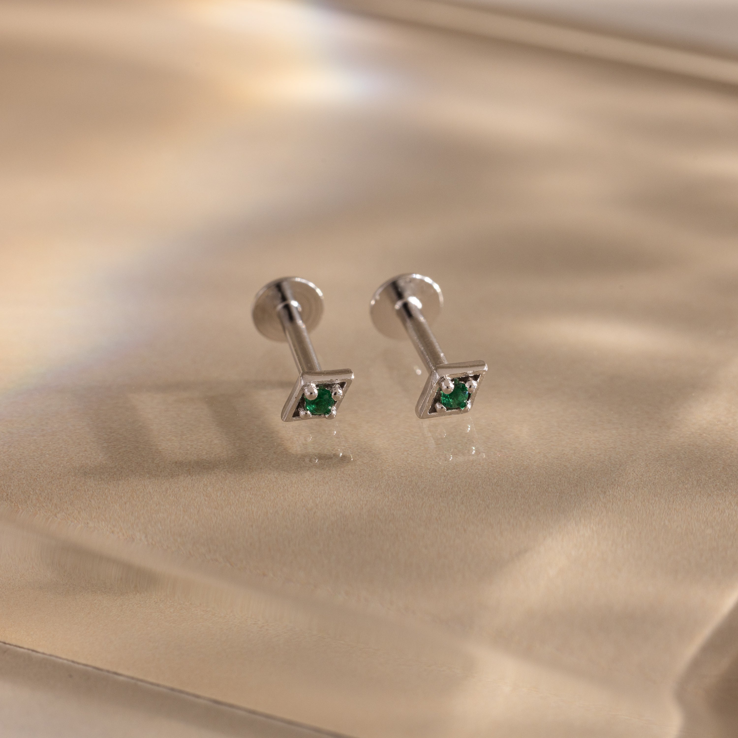 Pair of silver geometric flat back emerald stud earrings on a reflective surface