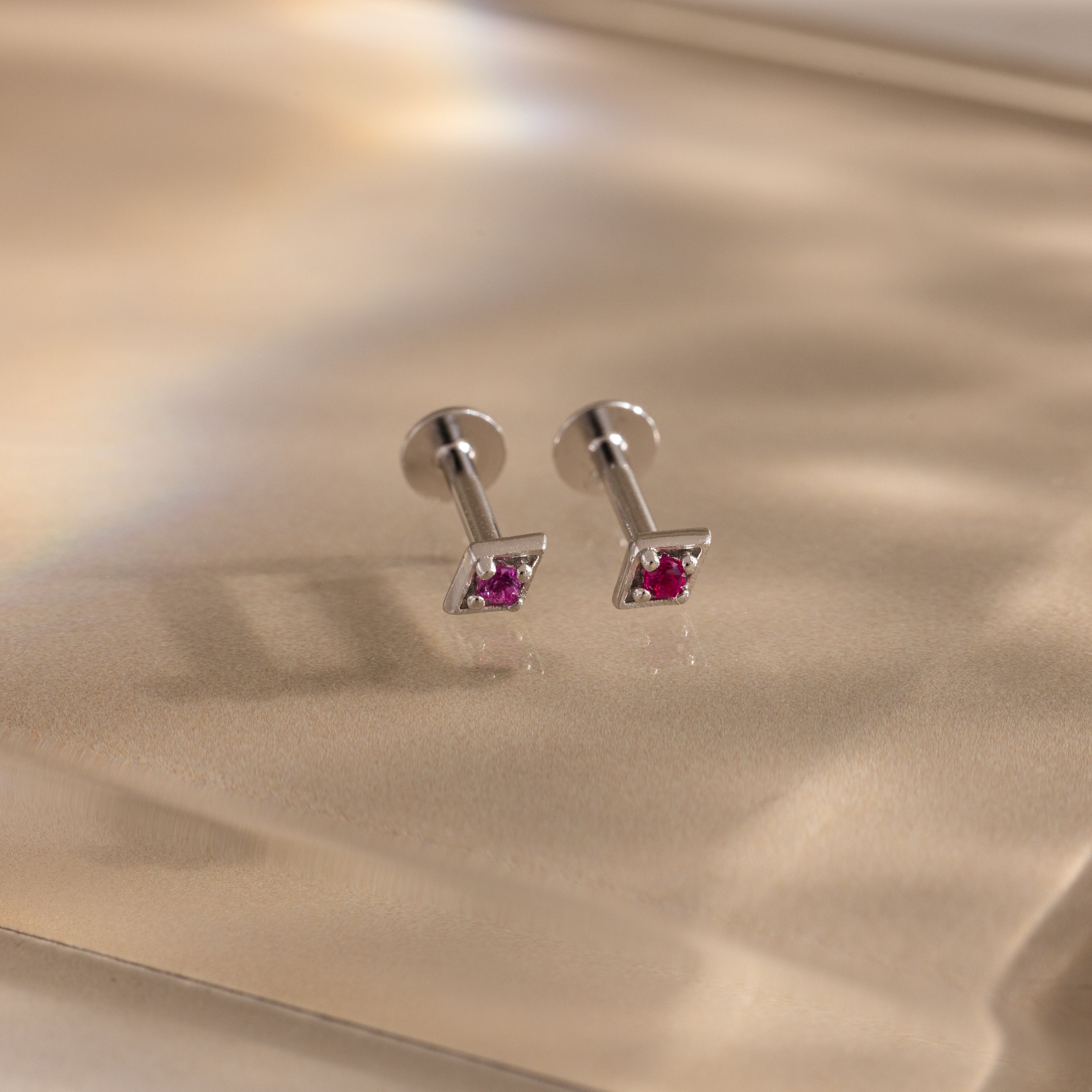 Pair of silver geometric flat back ruby stud earrings on a reflective surface