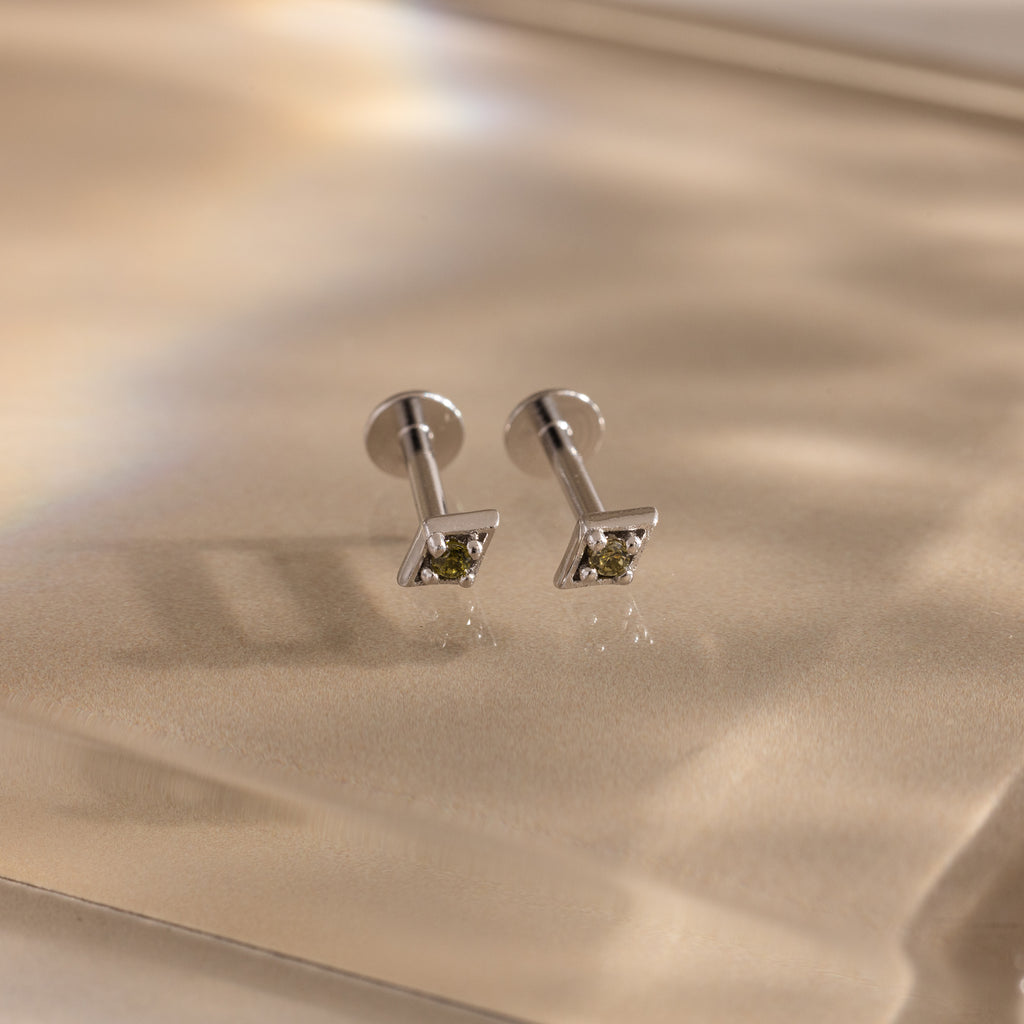 Pair of silver geometric flat back peridot stud earrings on a beige fabric background