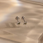 Pair of silver geometric flat back peridot stud earrings on a beige fabric background