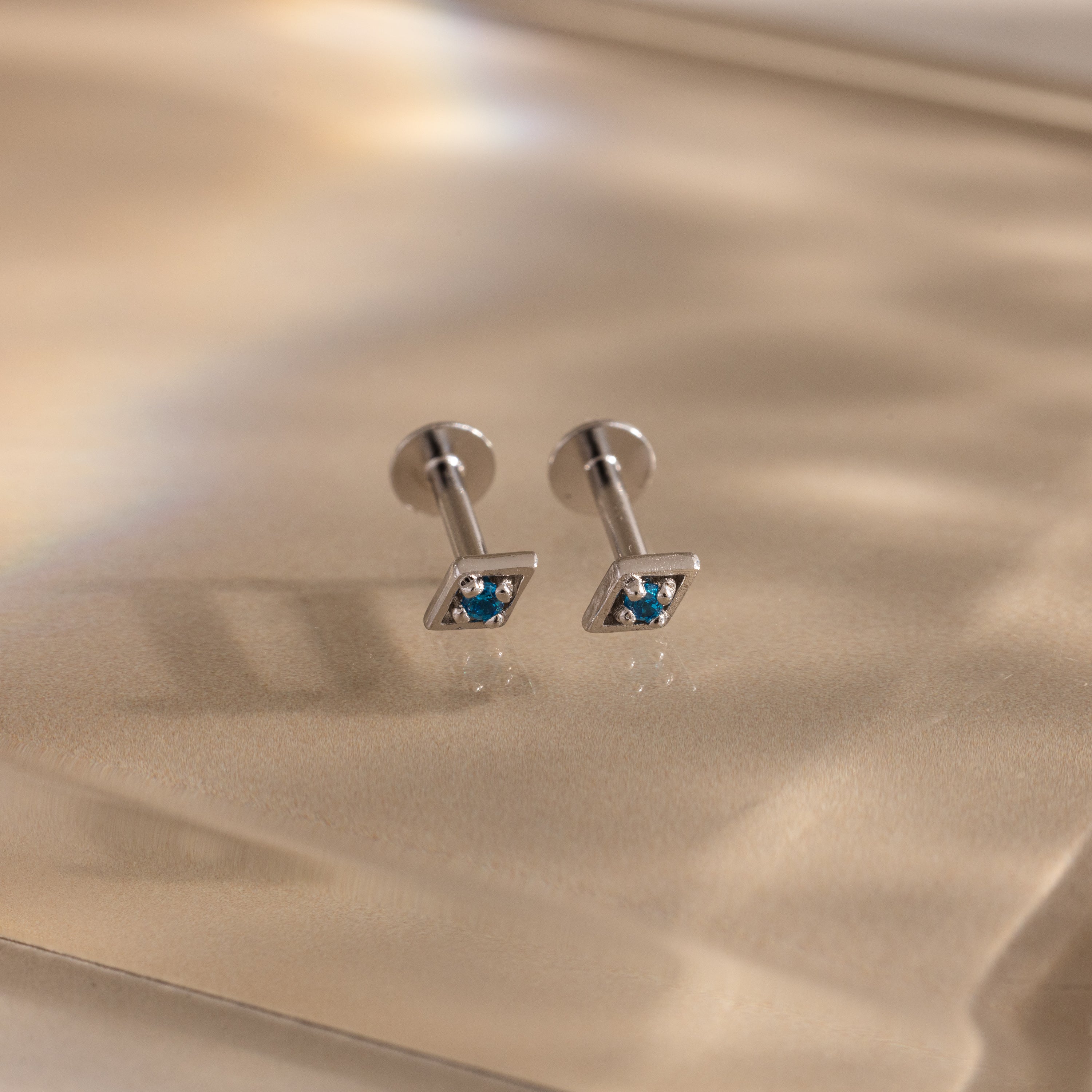 Pair of silver geometric flat back blue topaz stud earrings on a beige background