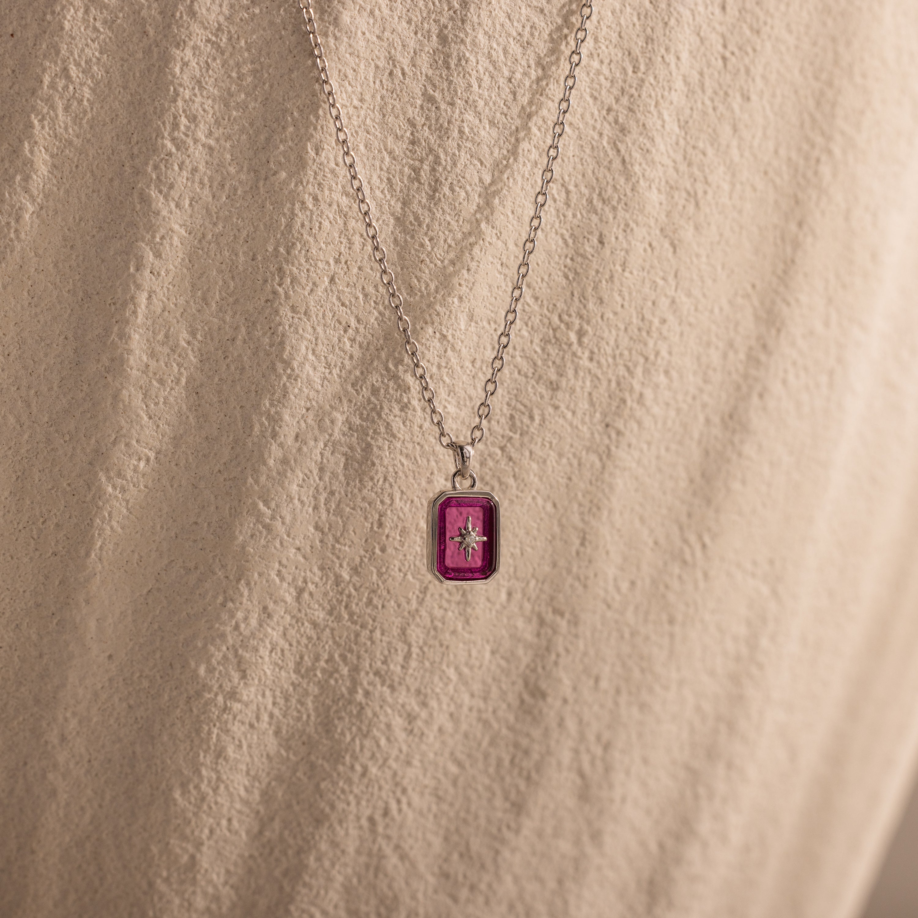 North Star Ruby Necklace featuring a rectangular pink crystal pendant, beautifully displayed against a textured beige background.