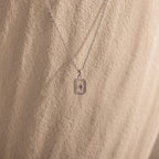 The North Star Diamond Necklace features a rectangular crystal pendant with a delicate diamond-set North Star design, showcased against a textured beige background.