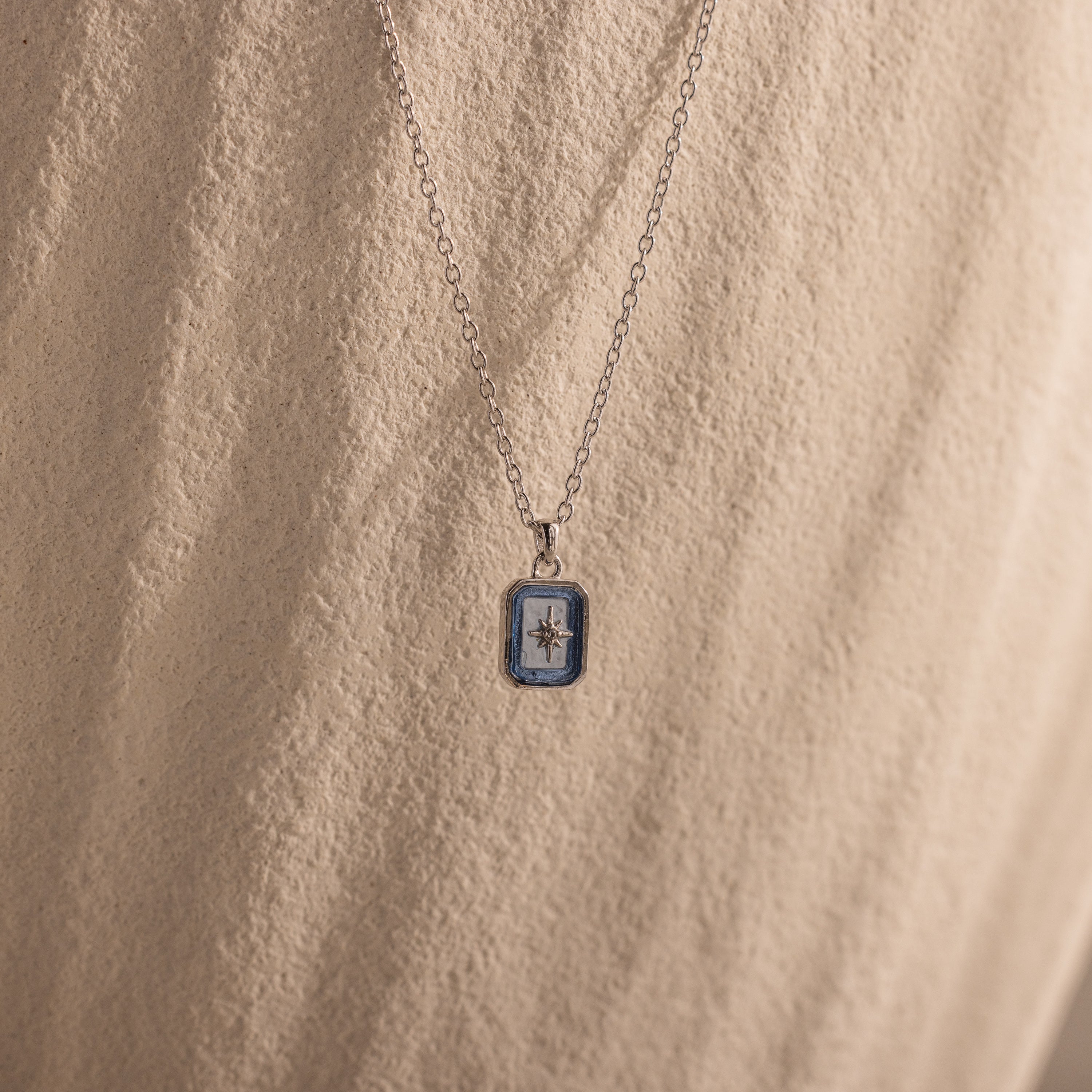 North Star Aquamarine Necklace with a small rectangular pendant and a North Star design, accented by aquamarine stones, set against a textured beige background.