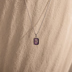 The North Star Amethyst Necklace, featuring a purple rectangular crystal pendant, is displayed on a textured beige background.