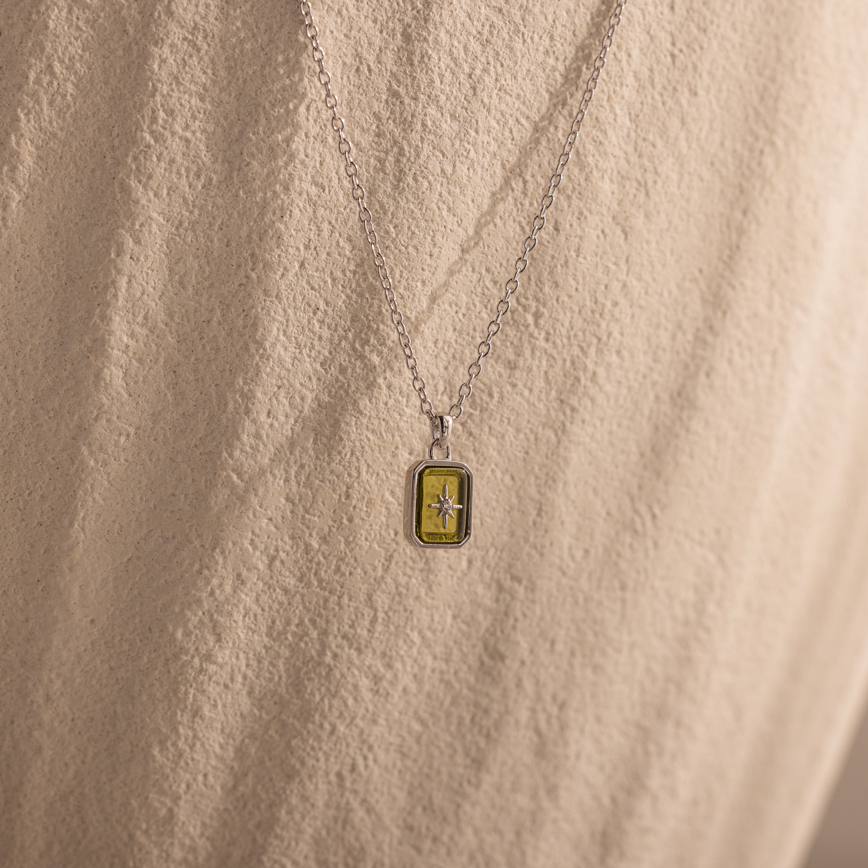 North Star Peridot Necklace featuring a small rectangular yellow crystal pendant, displayed on a textured, light-colored surface.
