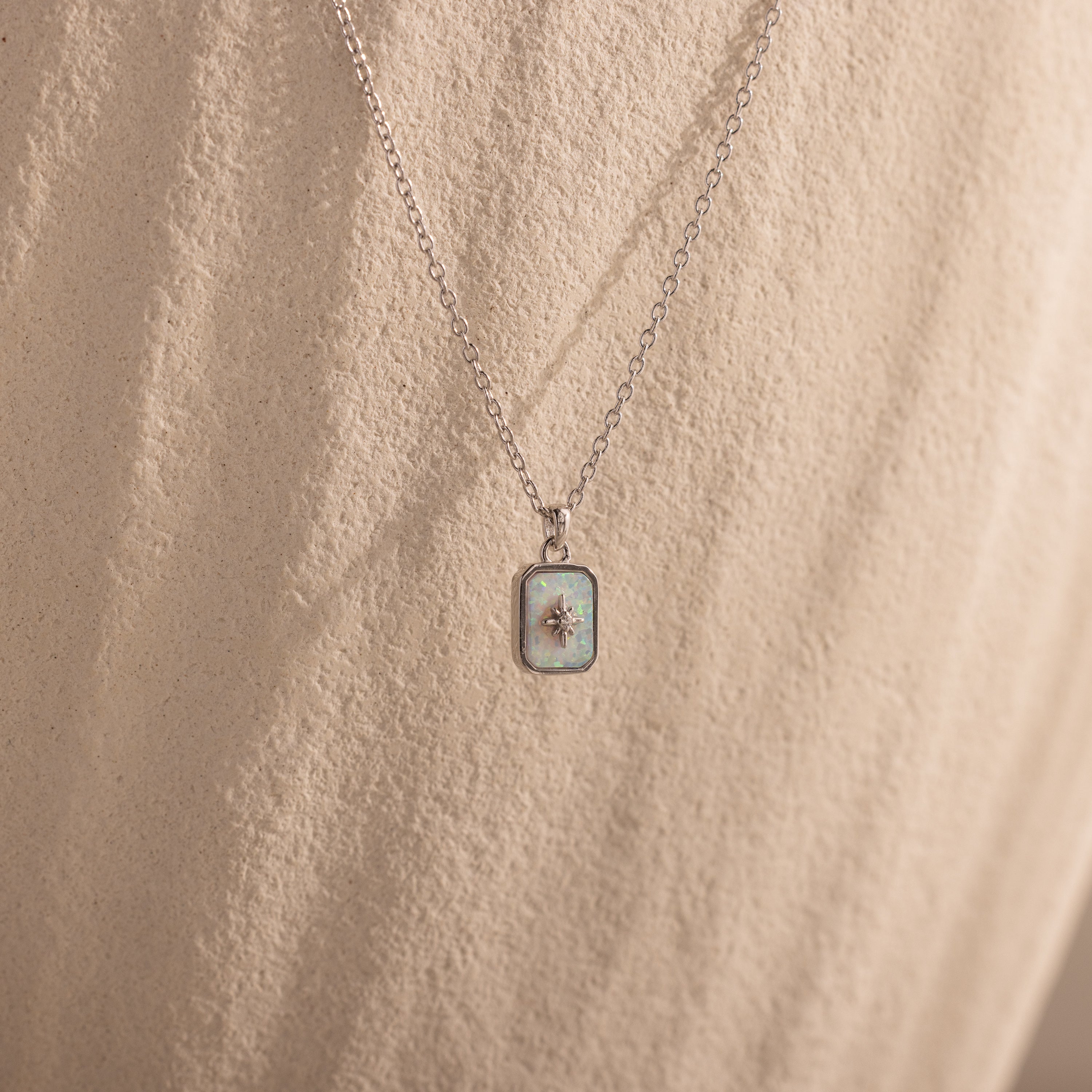 North Star Opal Necklace featuring a silver chain and opal pendant, displayed against a textured beige background.