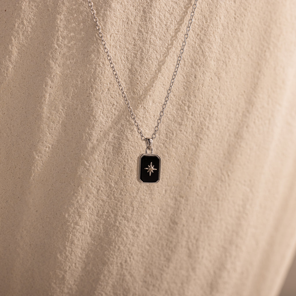 North Star Gemstone Necklace featuring a black rectangular pendant with a small star design, displayed on a textured beige background.