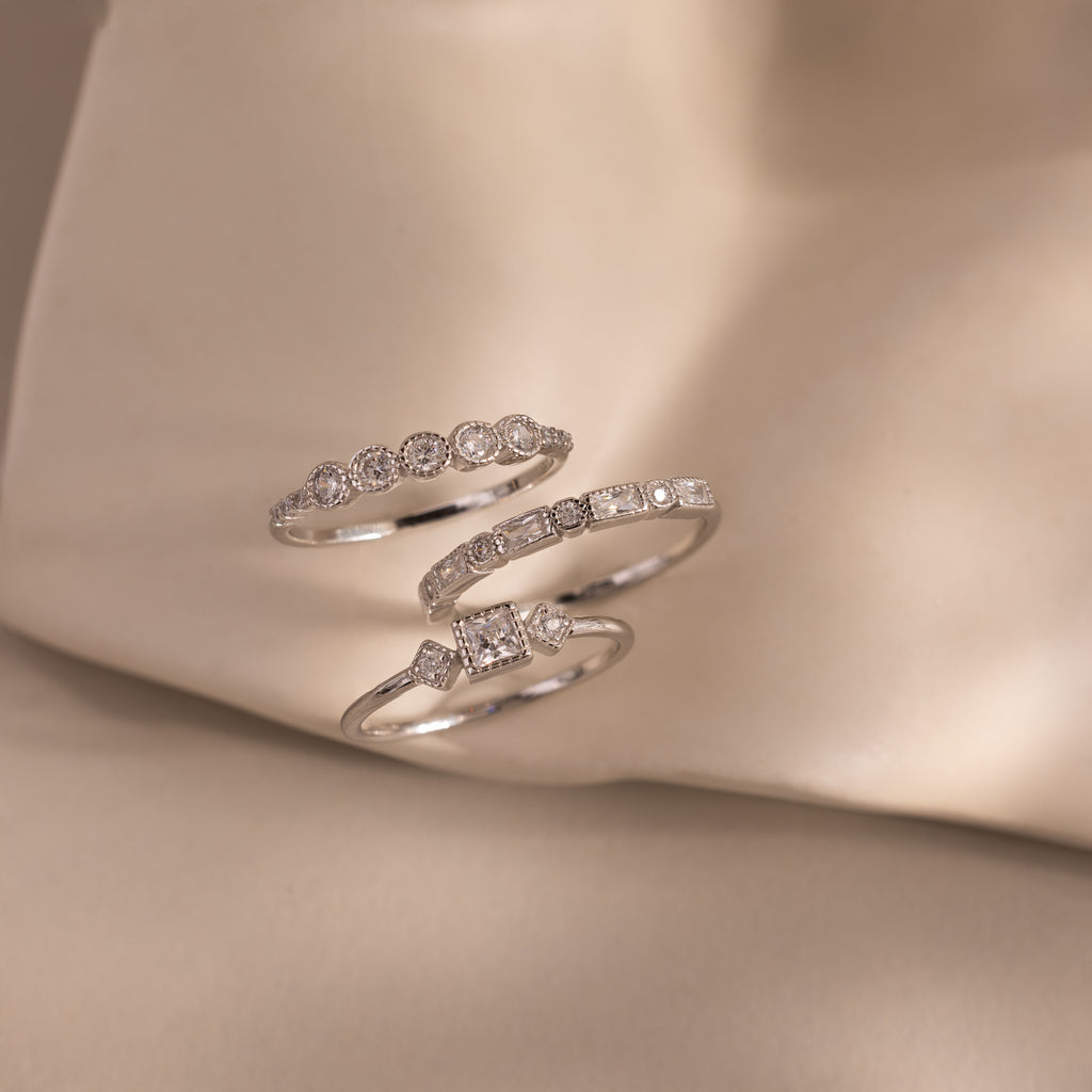 Three silver Art Deco rings with different diamond cuts displayed on a soft, beige fabric surface.